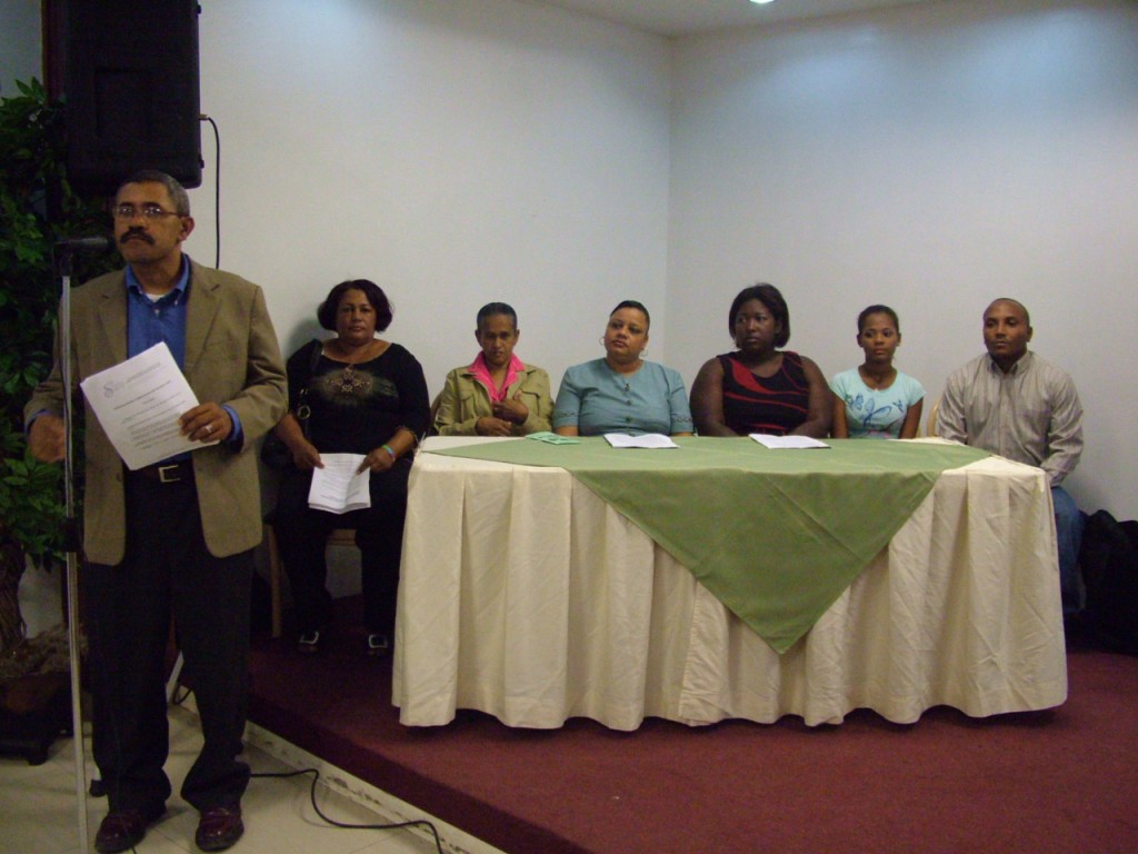 Mesa de Dialogo Mesa principal en la presentación de la Mesa de Dialogo y Concertación de Santa Lucía, de pies José Jáquez, sentadas de izquierda a derecha, Cecilia Angelina, Angelita Plasencia, Nurys Manuel, Rosa Silverio, Rosario Cabrera y Martín Delgado.